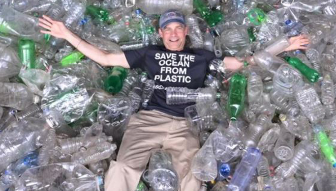 man laying in a bin of recycled plastic bottles.