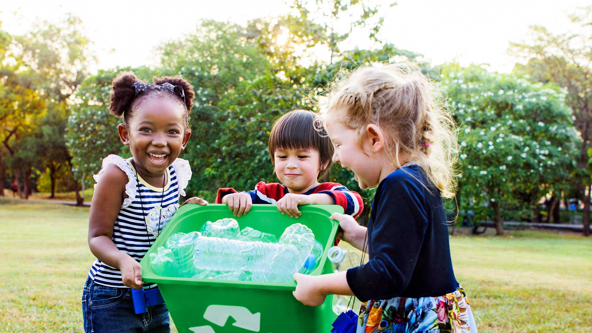 Bambini che raccolgono rifiuti riciclabili in un bidone verde. 