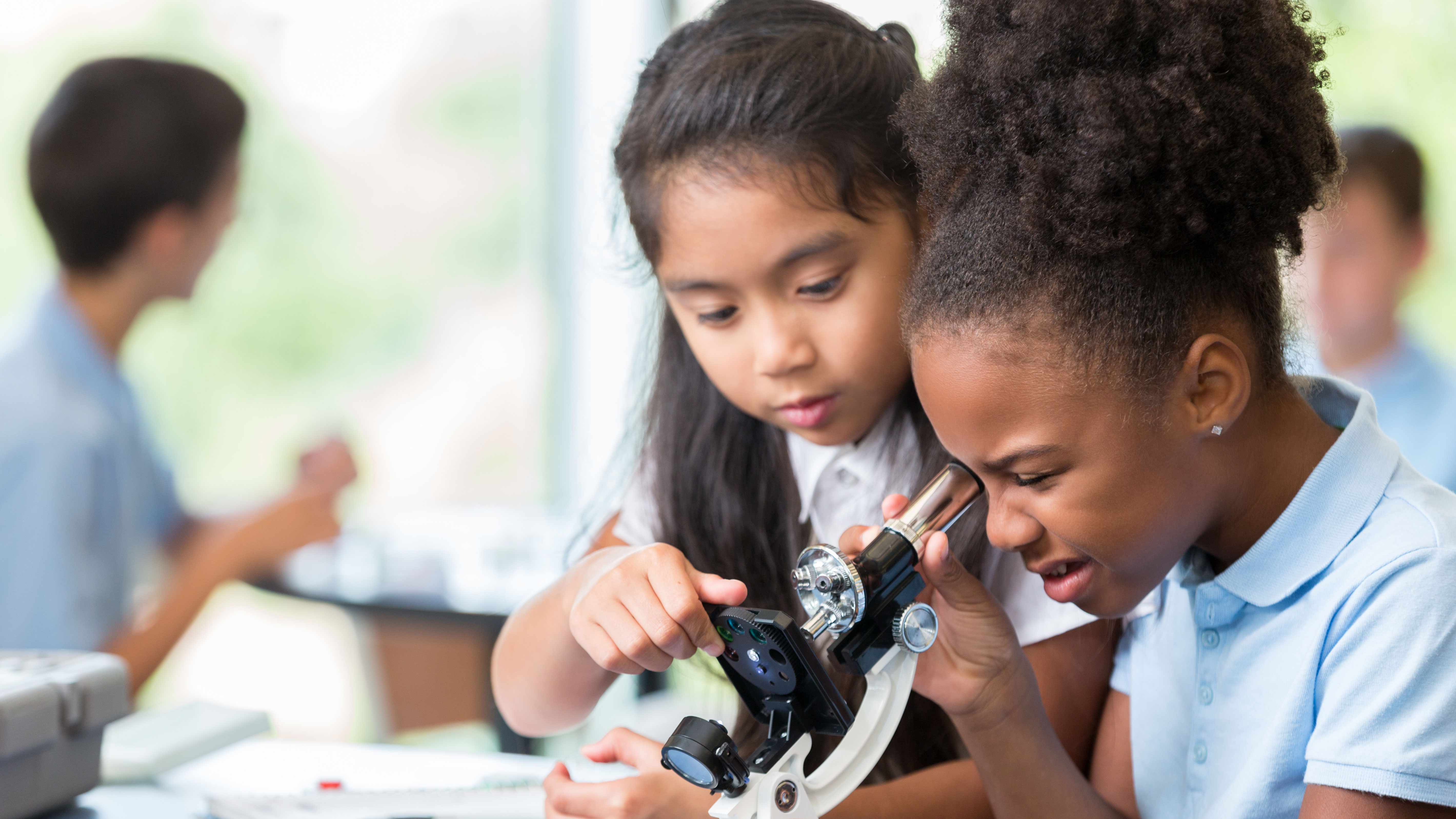 Young girls in science class looking into a microscope