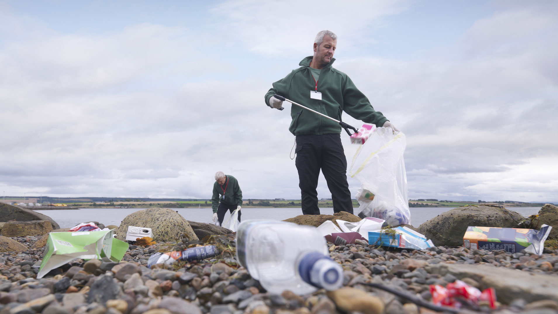 two men cleaning up garbage from the beach on a cloudy day